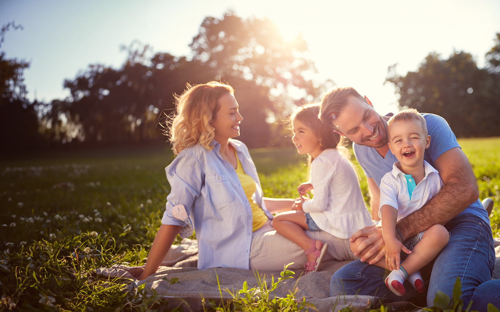 A family of four poses outdoors on a grassy field  an adult man and woman with two children, smiling and looking at the camera.