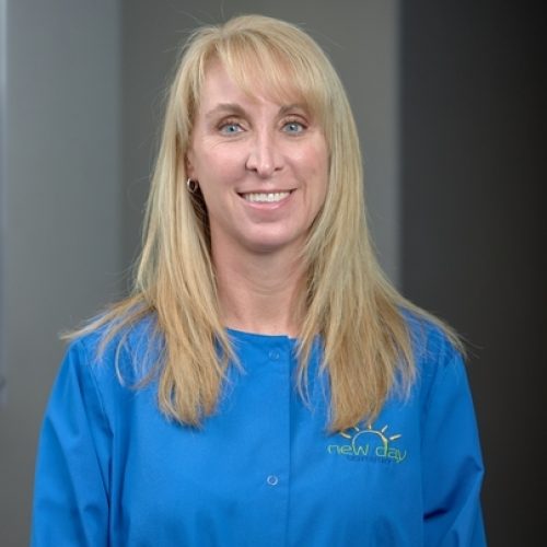 The image shows a woman with long hair wearing a blue lab coat standing indoors.