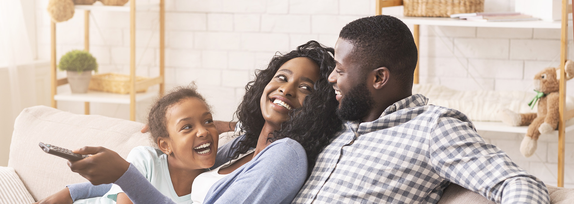 The image depicts a family of four sitting together on a couch, with two adults and two children, all smiling and enjoying each other s company.