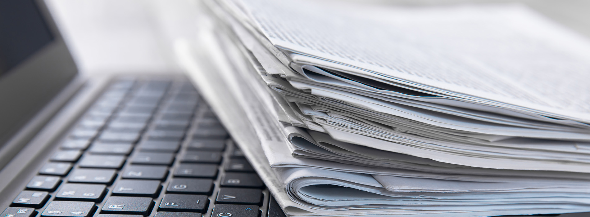 The image shows a stack of papers on top of a laptop computer, with a keyboard visible beneath the papers.