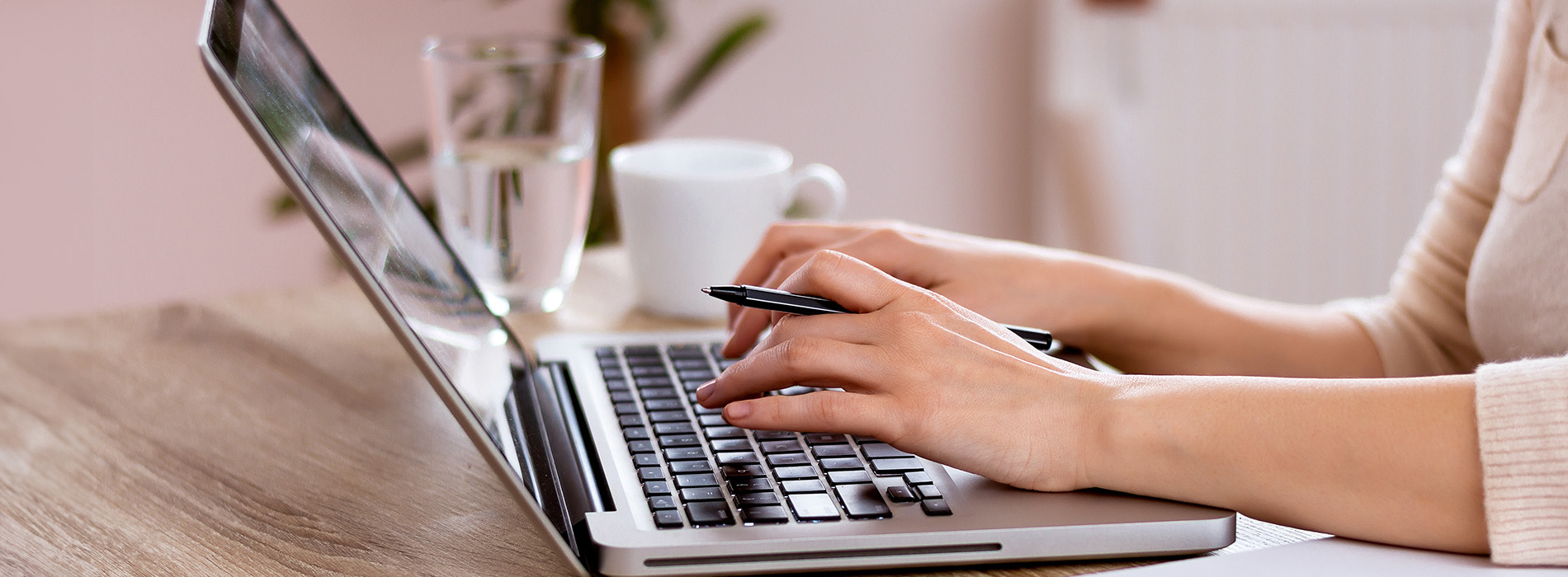 A person typing on a laptop computer at a desk with a blurred background.