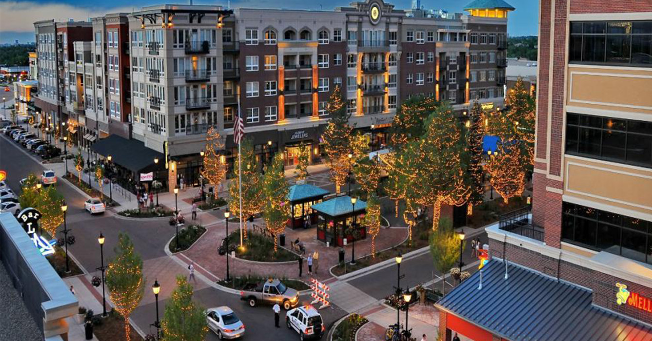 The image depicts a lively city street at night with illuminated buildings, trees, and parked cars, showcasing a festive atmosphere with holiday decorations and lights.