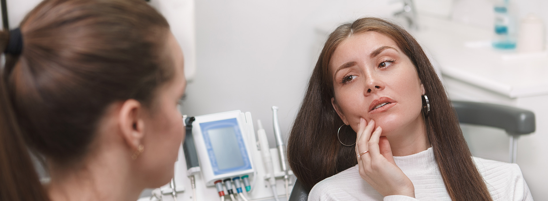 The image shows a woman seated with her eyes closed, receiving dental care from a professional who appears to be a dentist, while another person watches attentively.