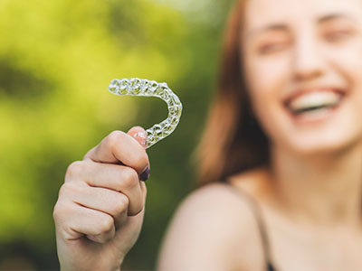 A smiling woman holding a clear plastic mouthguard with her right hand.