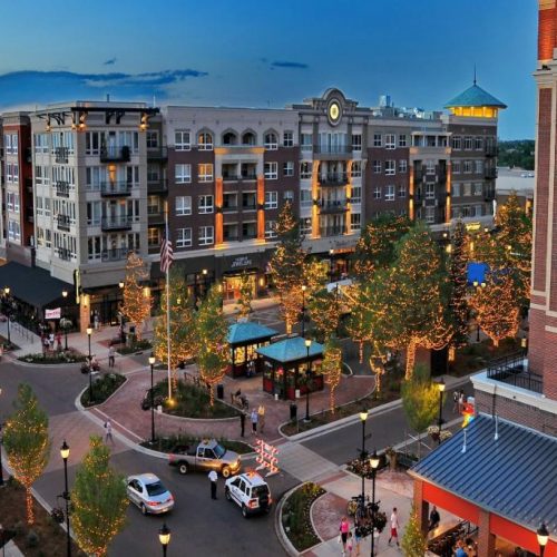 The image depicts a vibrant city street at dusk, with illuminated buildings, trees adorned with lights, and holiday decorations lining the sidewalks.