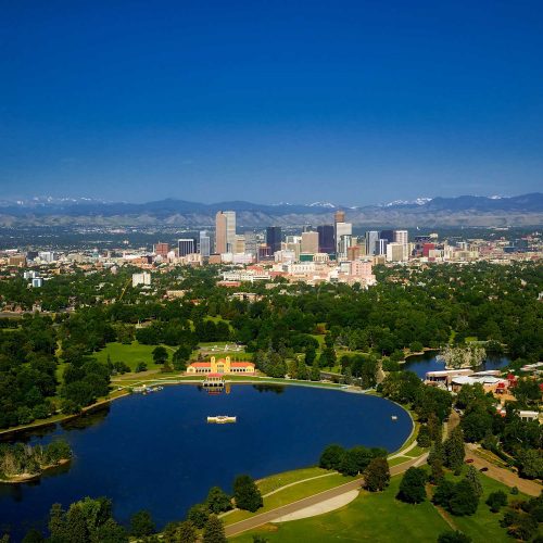 The image depicts an aerial view of a city with a prominent lake, surrounded by mountains, under a clear blue sky.