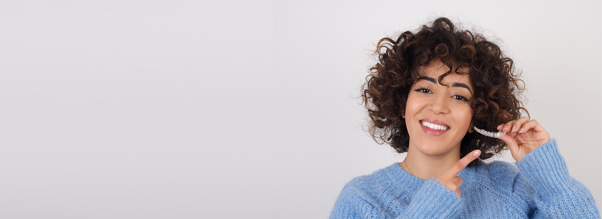 The image shows a person with curly hair smiling and holding a toothbrush. They are wearing a blue sweater, and there s a watermark on the photo that reads  lucy_jane.