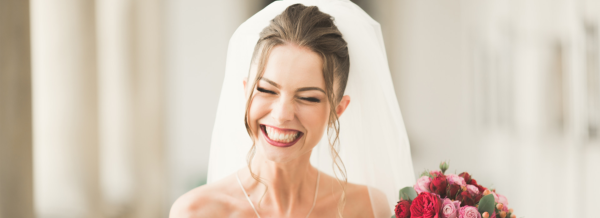 The image features a bride smiling at the camera with a bouquet of flowers behind her, wearing a traditional wedding veil and holding a bouquet of roses.