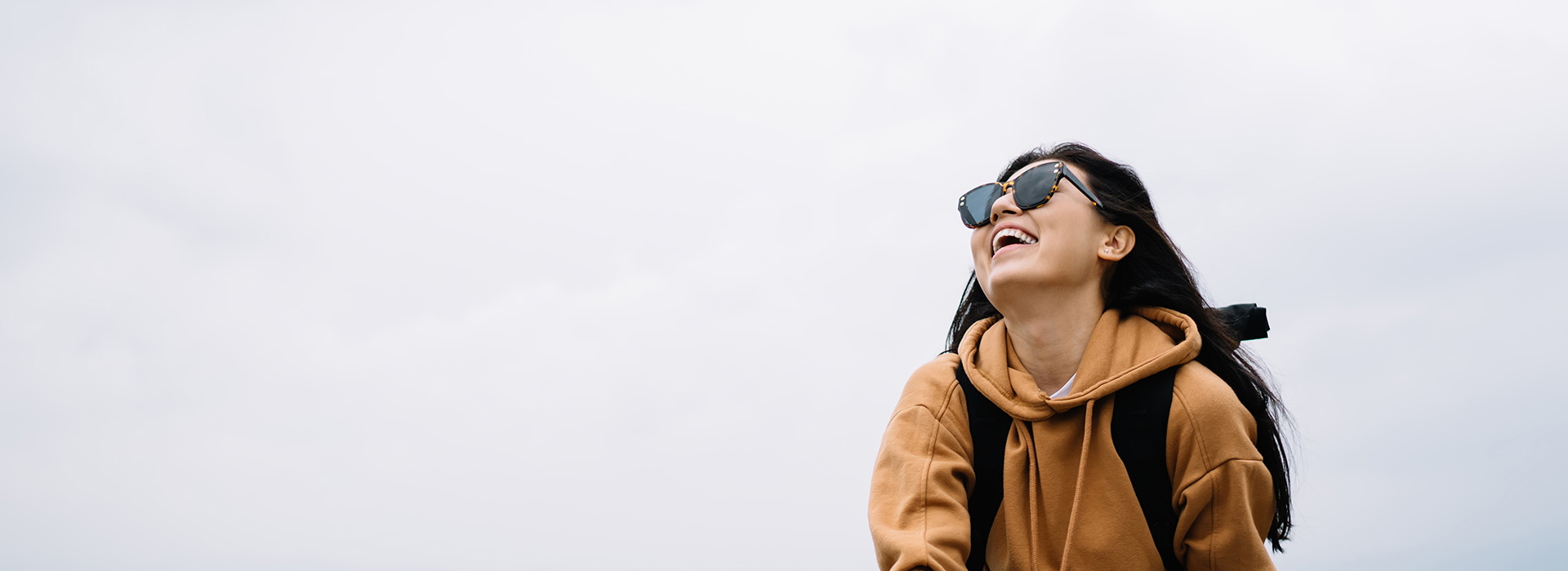 Woman wearing sunglasses and backpack, smiling at camera while standing outdoors.
