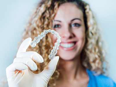 The image shows a person holding up a clear plastic tray with a single round object inside, which appears to be a dental implant, against a white background.