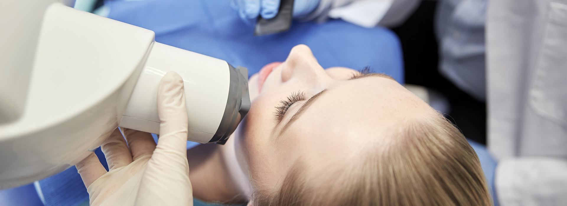 A woman receiving facial treatment under a magnifying device, with a medical professional s hand visible holding a tool.