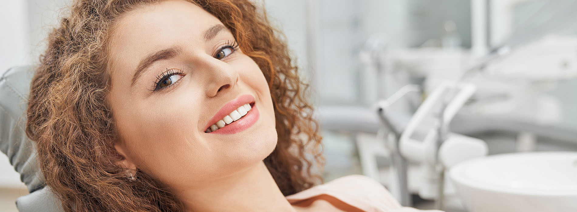 A woman with curly hair smiling towards the camera while sitting in a dental chair.