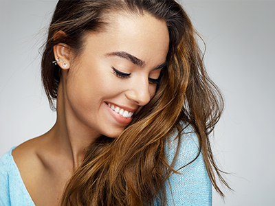 A split-image portrait of a smiling woman with long hair, wearing a blue top, against a white background.