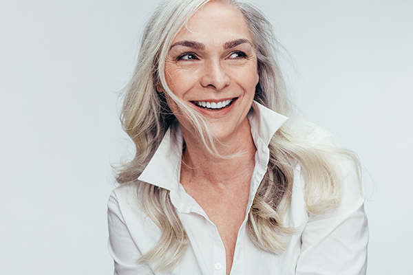 The image shows a woman with short hair smiling at the camera while wearing a white shirt.