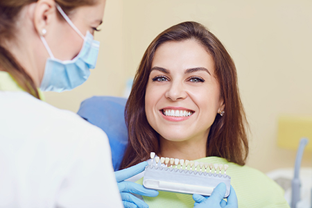 A woman sitting in a dental chair with a smile on her face while a dentist checks her teeth.