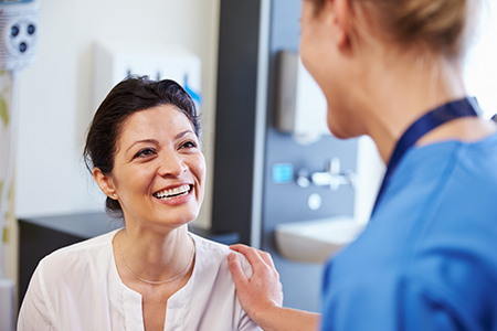 A woman with a smile stands next to a nurse in a medical setting, both appear engaged in conversation.