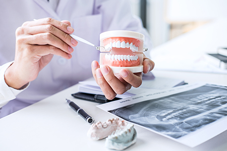 The image shows two different scenes  on the left, a dentist holding a tooth model with a magnifying glass  on the right, a hand holding a cup with dental implants.