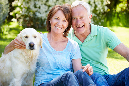 An elderly couple sitting outdoors with their golden retriever dog.