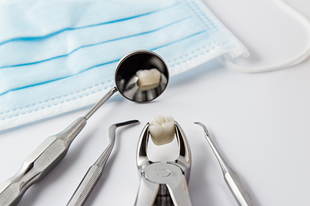 The image shows a dental tool set with a toothbrush inside a sterilization container, placed on a white surface, next to a blue surgical mask.