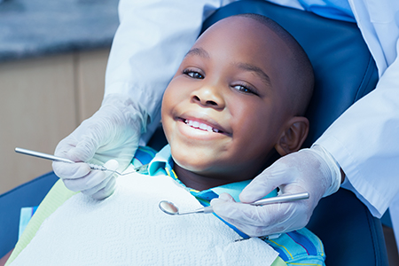 A young boy sitting in a dental chair at a dentist s office, smiling broadly while receiving dental care.