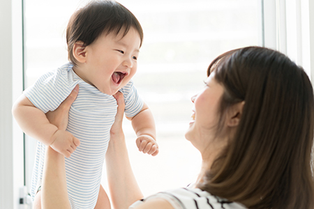 A woman holding a baby while smiling, with both looking at the camera.