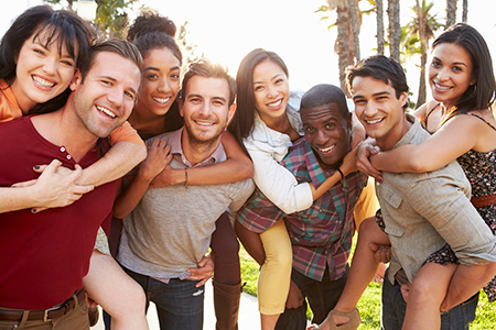 A group of people are posing together for a photo with smiles on their faces, standing outdoors during daytime.