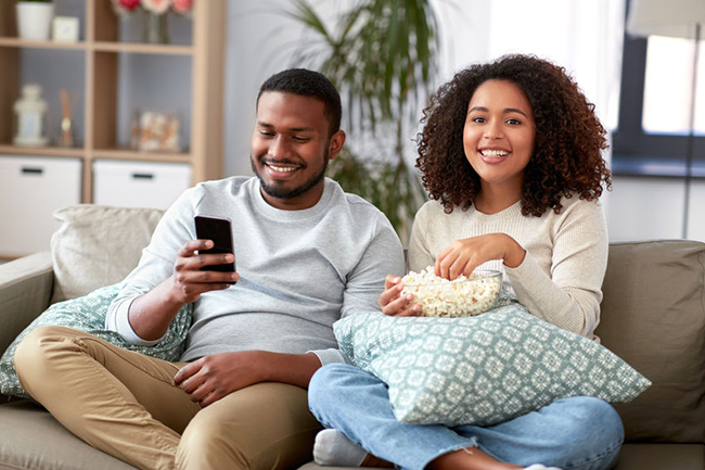 A man and woman sitting on a couch, enjoying a movie together, with popcorn in front of them.