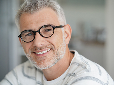 A man with glasses and a beard, smiling and looking directly at the camera.