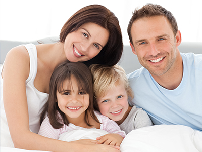An image of a family of four posing together on a bed with smiles, featuring an adult couple and their two children.