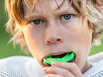 A split-screen photograph showing two different expressions of a young male with an exaggeratedly large mouth holding a green object, possibly a whistle or a toy.