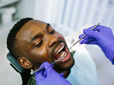 A man receiving dental treatment with a dentist using a drill on his teeth.
